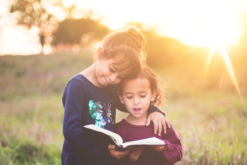 Photo by Ben White girl's left hand wrap around toddler while reading book during golden hour